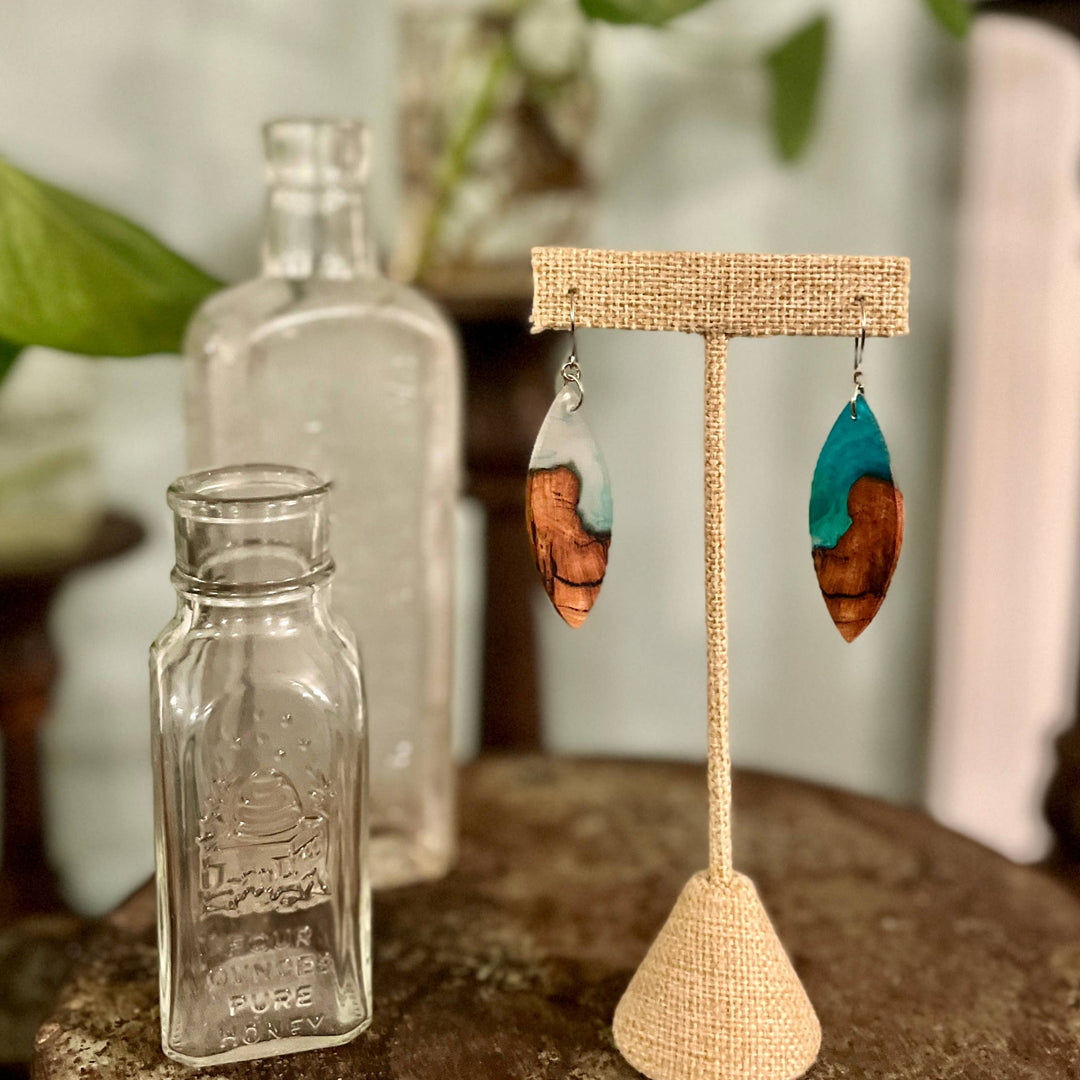 Wooden earring stand with wooden earrings on a table with greenery in the background