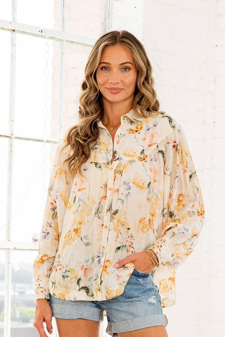 Woman wearing cream watercolor floral button-down blouse with long sleeves and denim shorts