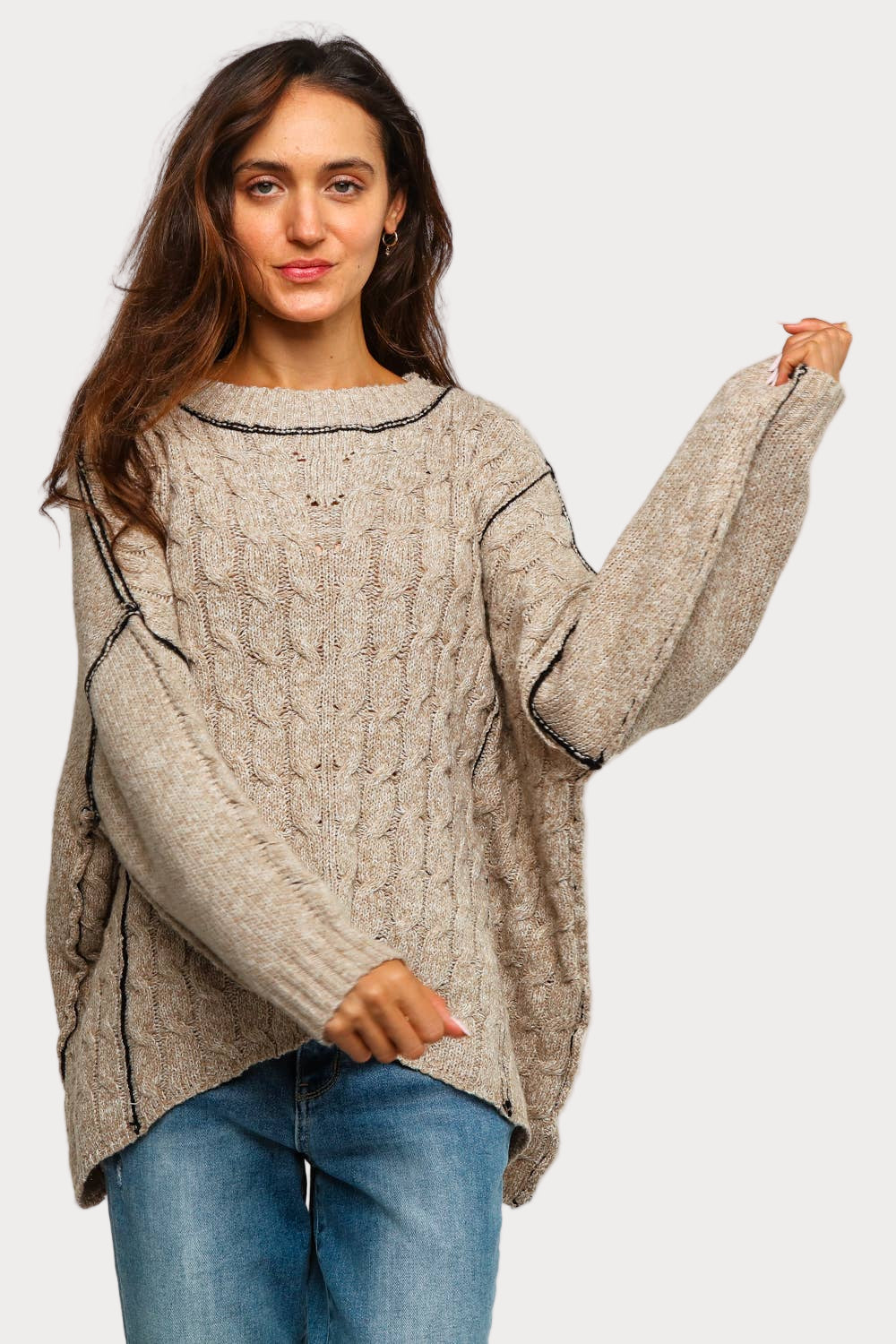Woman wearing a beige cable knit sweater with black contrast stitching and relaxed fit, available in plus sizes 1X–3X.
