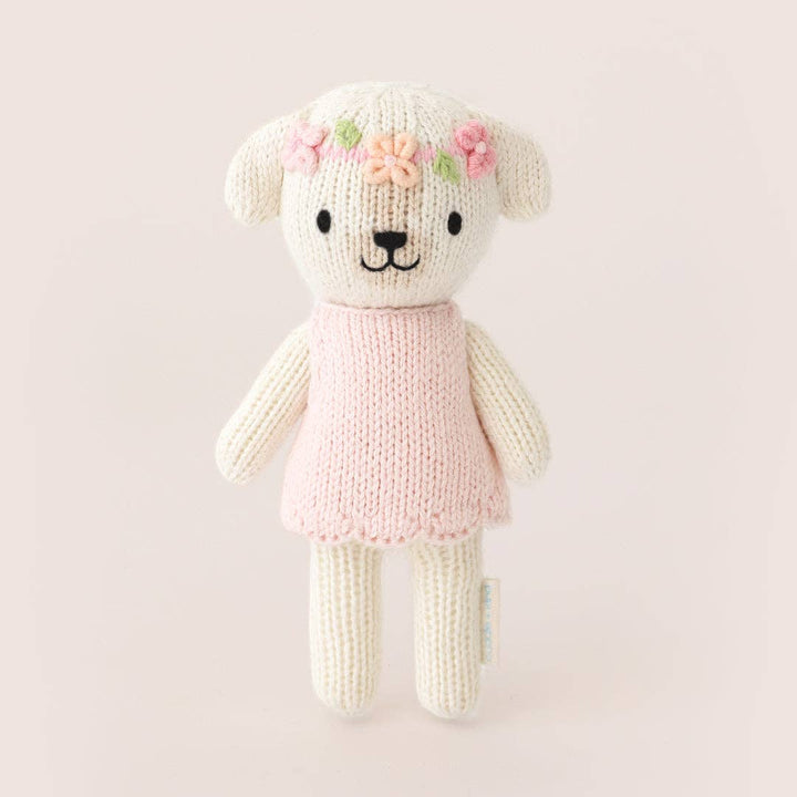 Knitted dog with a pink dress and floral headband on a light pink background