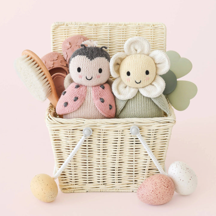 Two knitted toys, a ladybug and a flower, in a wicker basket on a pink background.