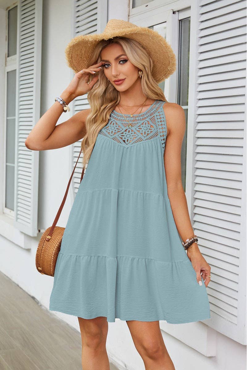 Woman wearing a light blue dress with lace details and a straw hat, standing in front of a white building.
