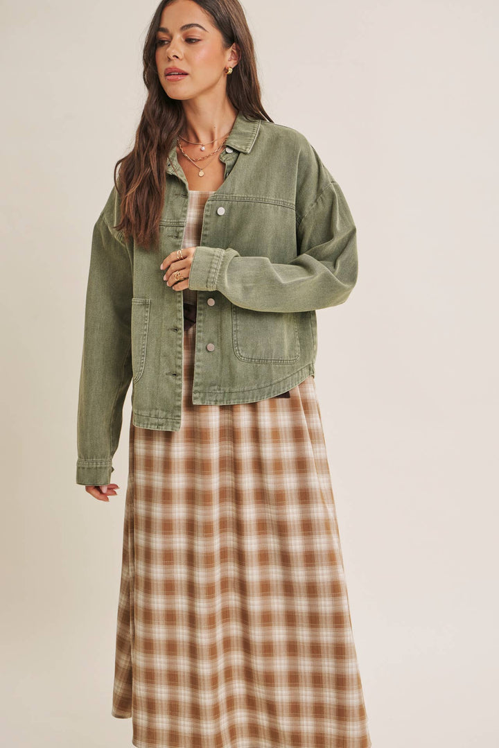 Woman wearing a olive green jacket over a plaid dress on a beige background