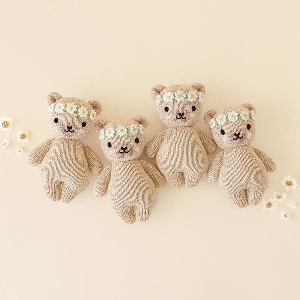 Four knitted teddy bears with floral headbands on a light beige background