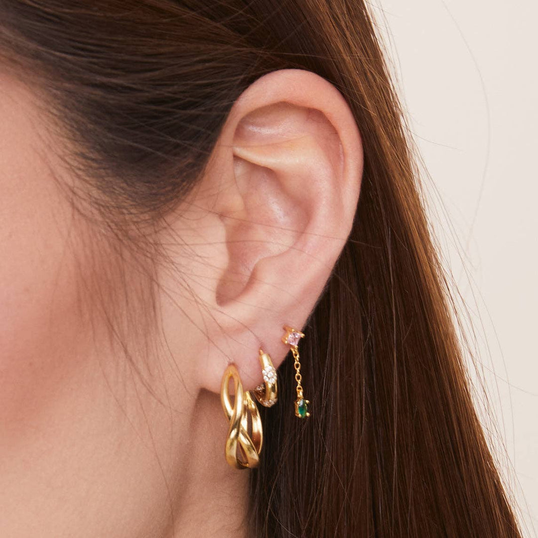 Close-up of an ear wearing gold hoop earrings with gemstones.