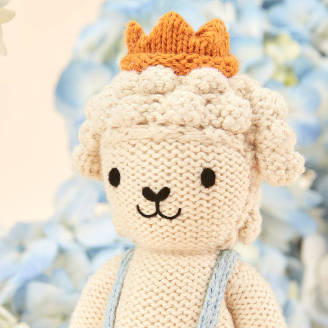 Knitted toy lamb with a crown against a blurred natural background