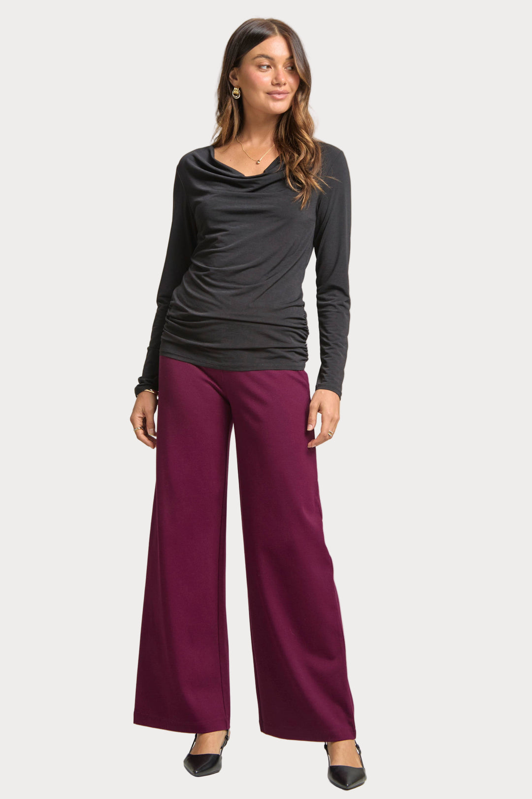 Woman wearing a black long-sleeve top and purple pants on a plain background