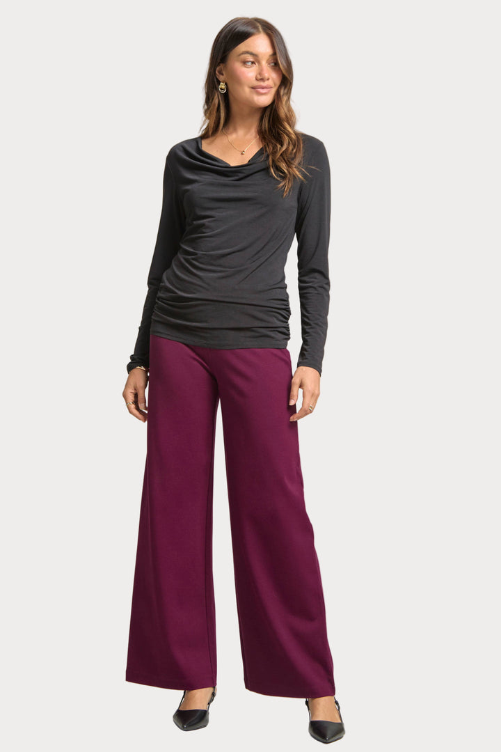 Woman wearing a black long-sleeve top and purple pants on a plain background