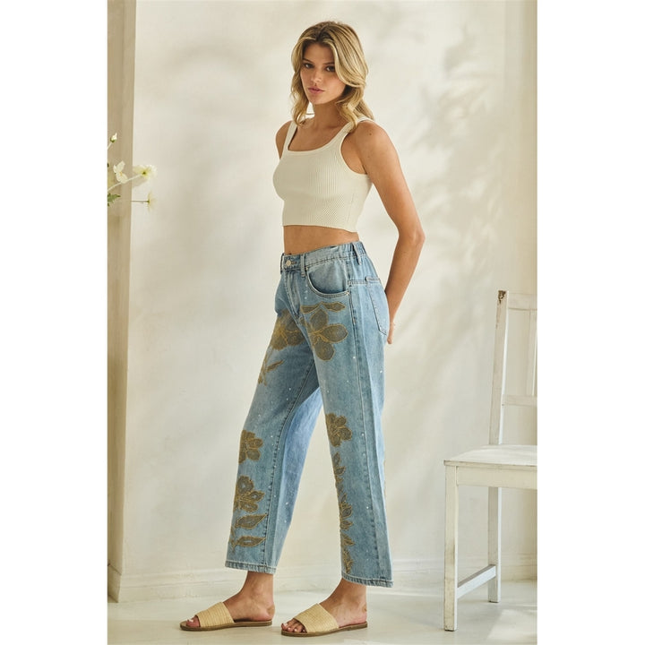 Woman wearing a white tank top and floral jeans in a room with a chair and door.