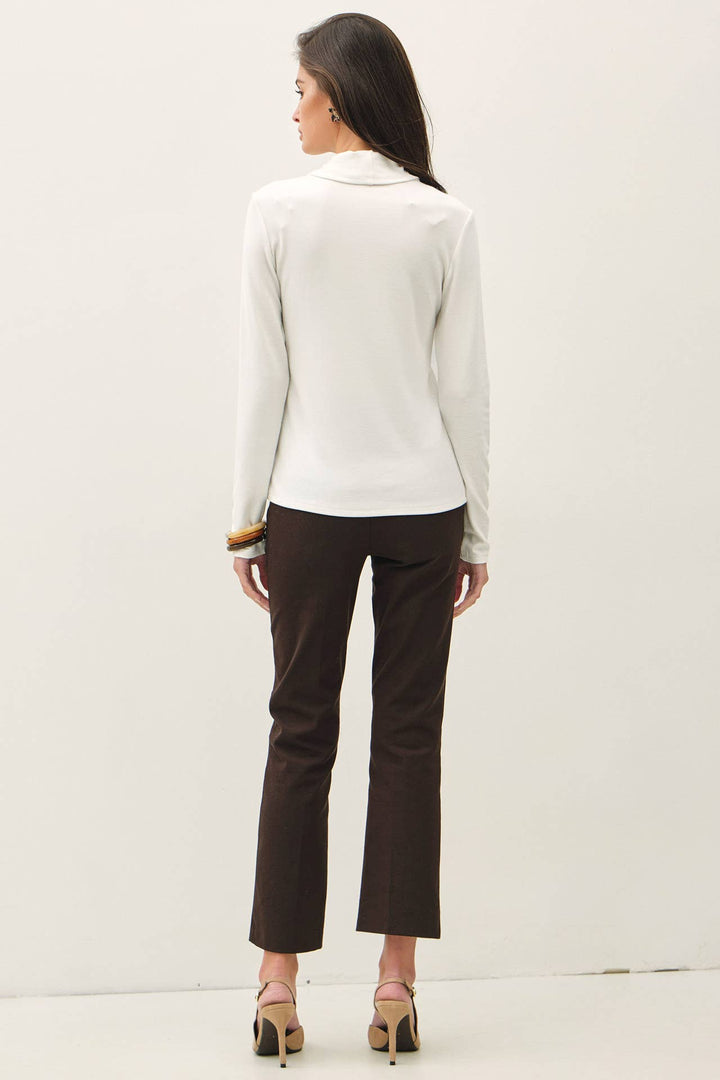 A woman shown from the back wearing a white long-sleeve turtle neck top, dark brown cropped trousers, and beige high heels against a plain white studio background.