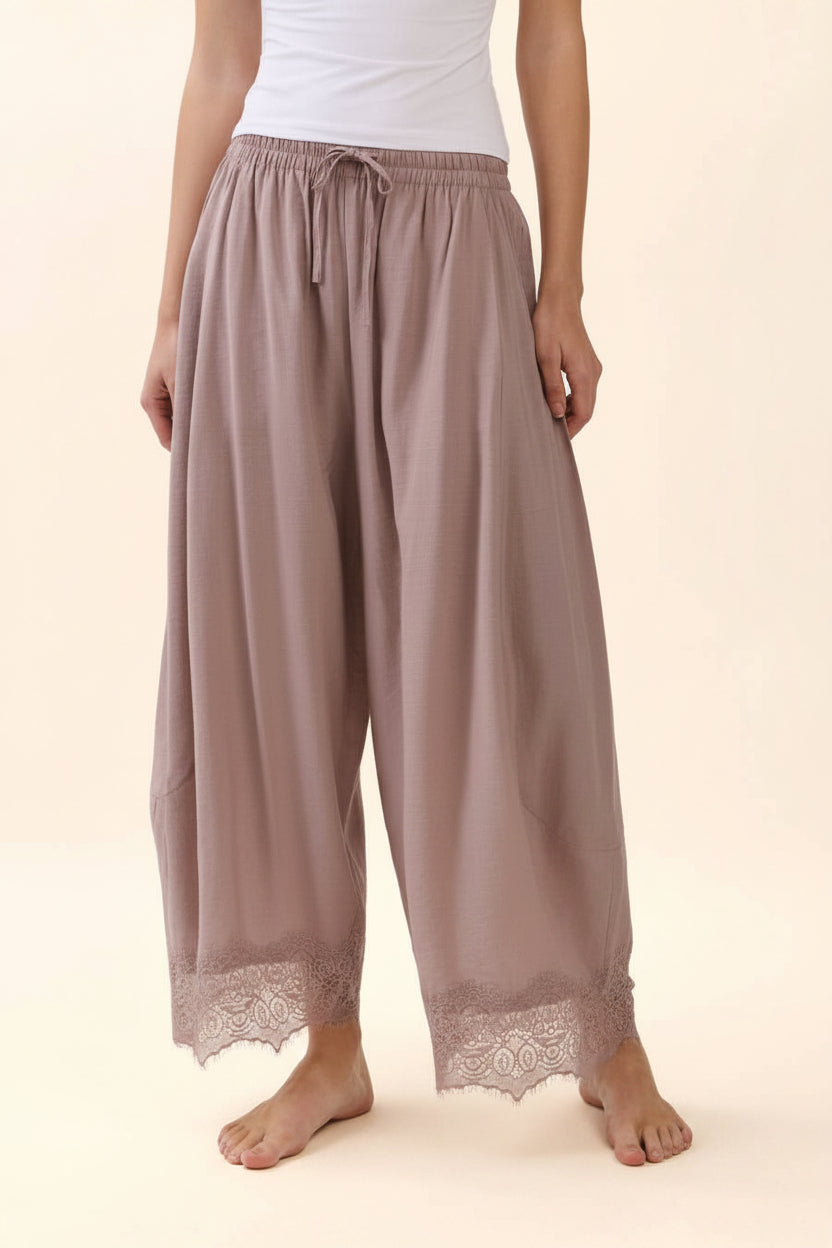 Woman wearing dusty rose crinkled wide-leg pants with an elastic drawstring waistband and delicate lace trim hem.