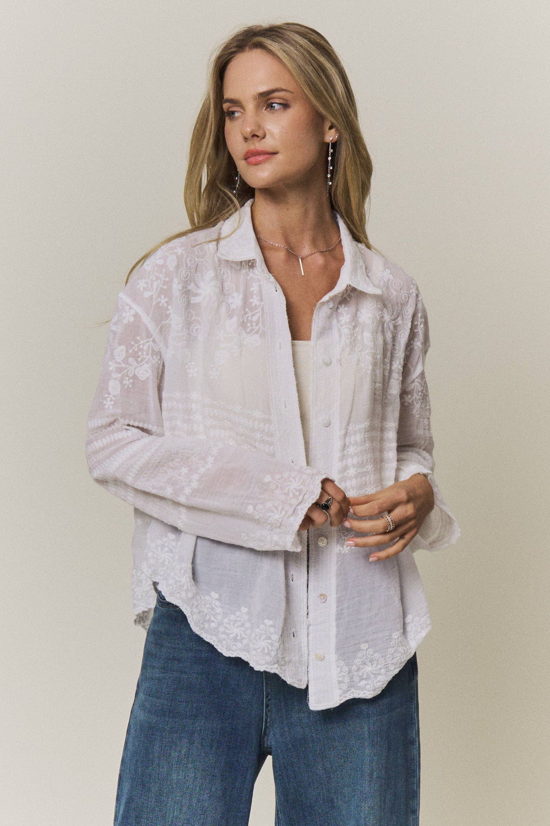 Woman wearing a light-colored lace embroidered blouse and blue jeans against a plain background