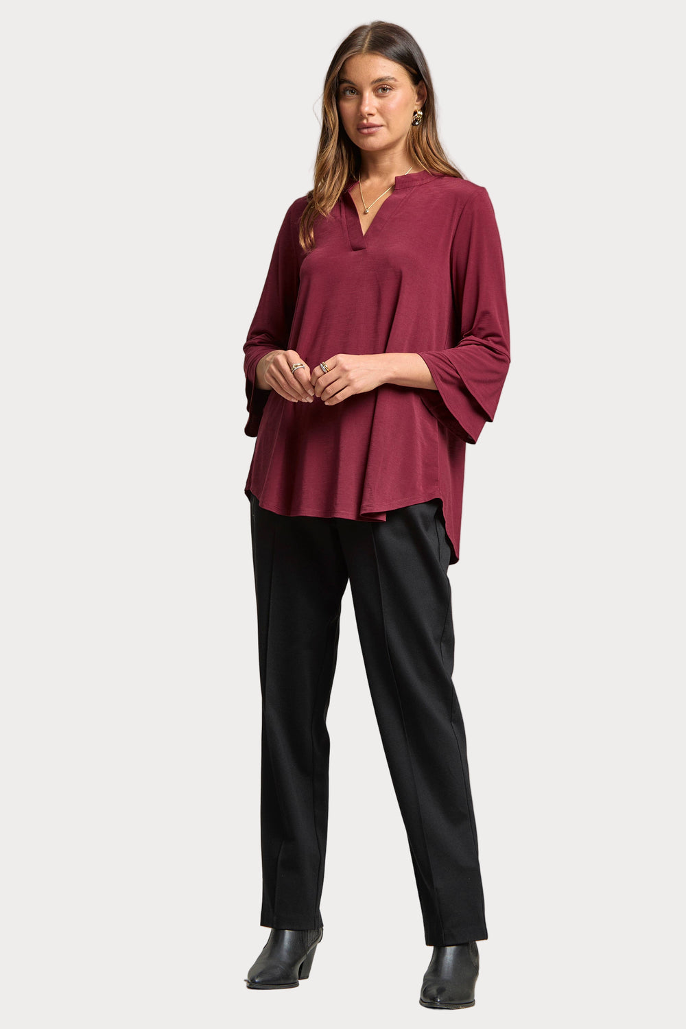 Woman wearing a burgundy top and black pants on a plain background