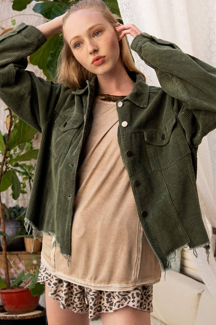 A woman models a relaxed-fit, olive green corduroy jacket with a raw, frayed hem over a tan t-shirt and leopard print shorts.

