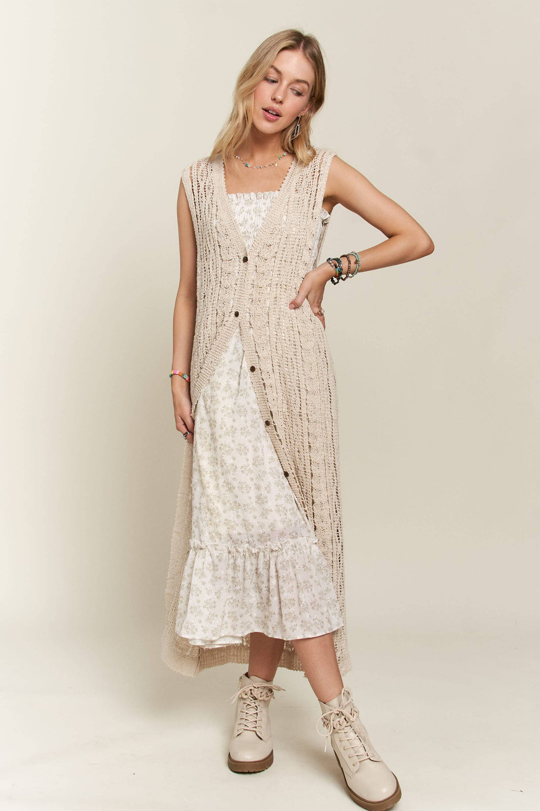 Woman wearing long beige crochet duster vest over a white floral dress
