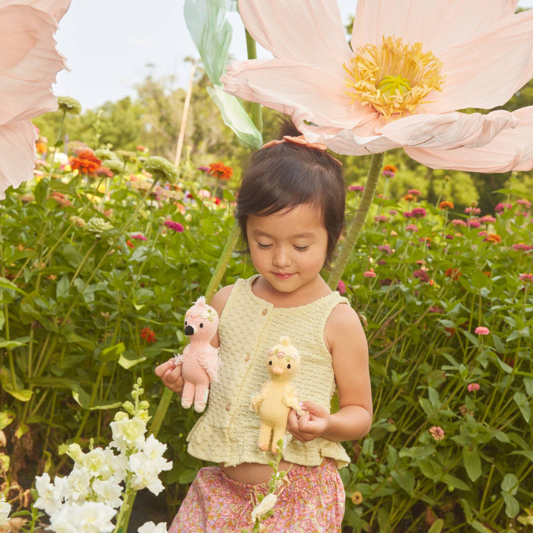 Young girl holding toys in a garden with large pink flowers
