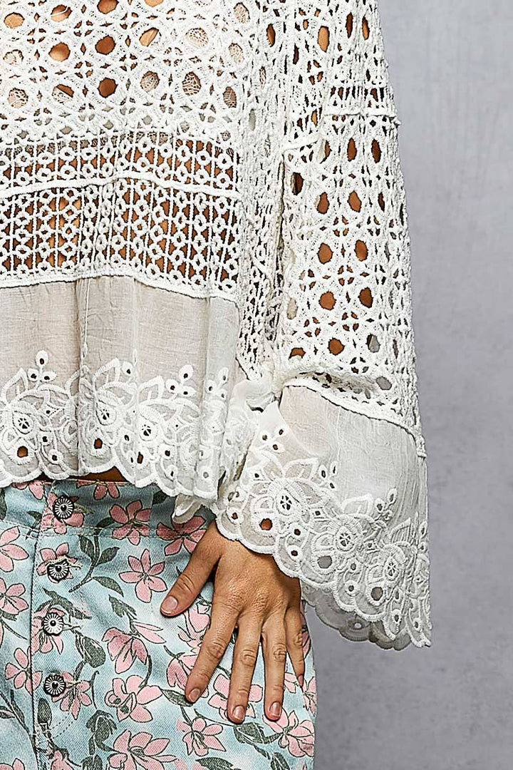 Model wearing The Briar Rose Crochet Blouse featuring intricate open crochet, embroidered eyelet cotton panels, long bell sleeves, and a relaxed bohemian silhouette in ivory.