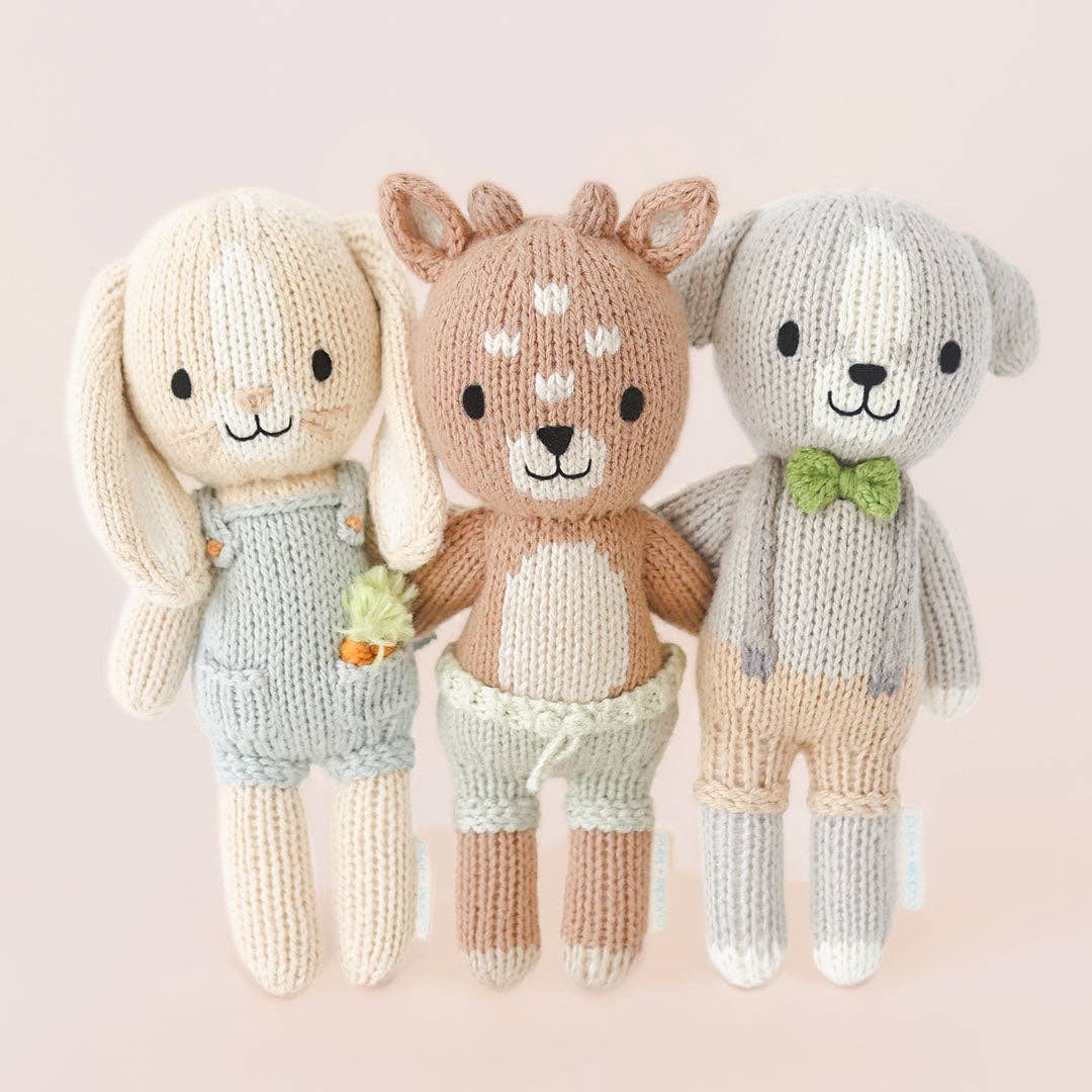 Three knitted toys resembling a rabbit, deer, and dog on a light pink background