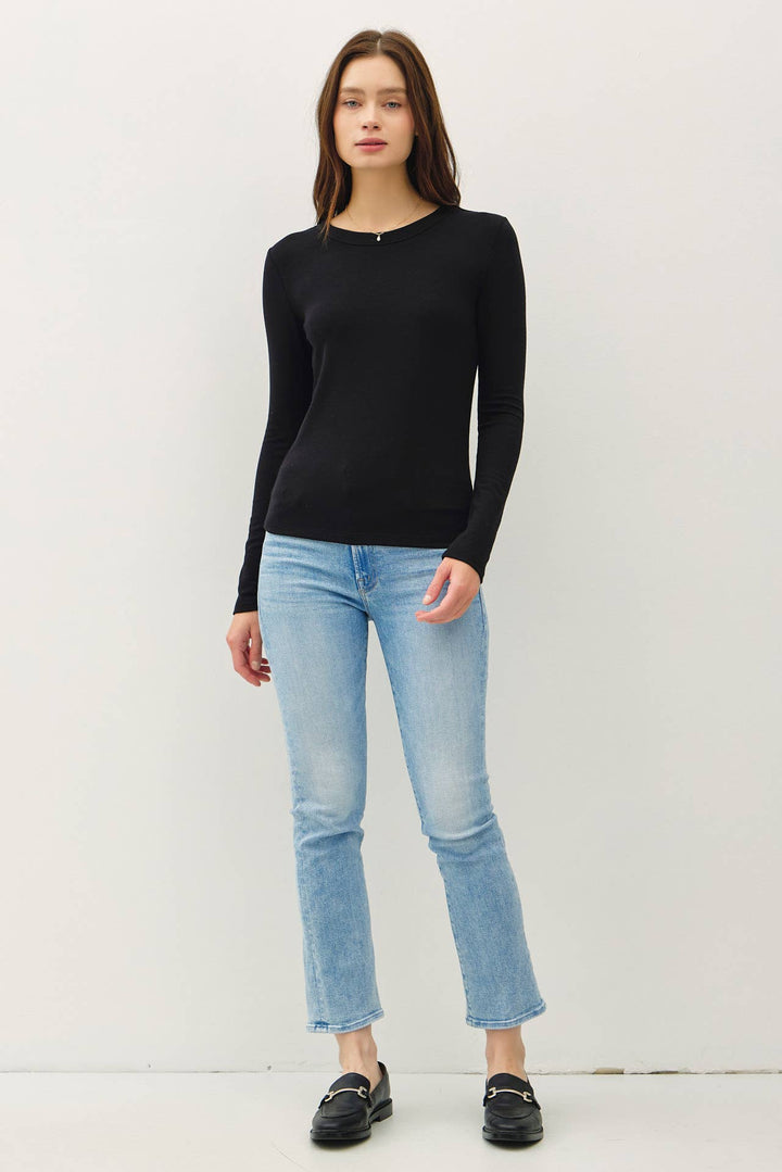 Woman wearing a black long-sleeve top and light blue jeans against a white background