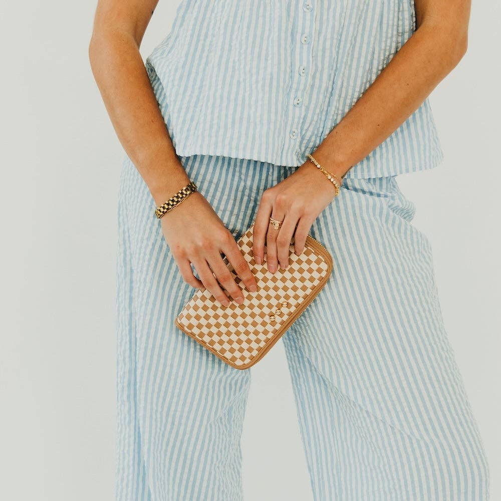 Person holding a tan & cream checkered clutch bag against a light background