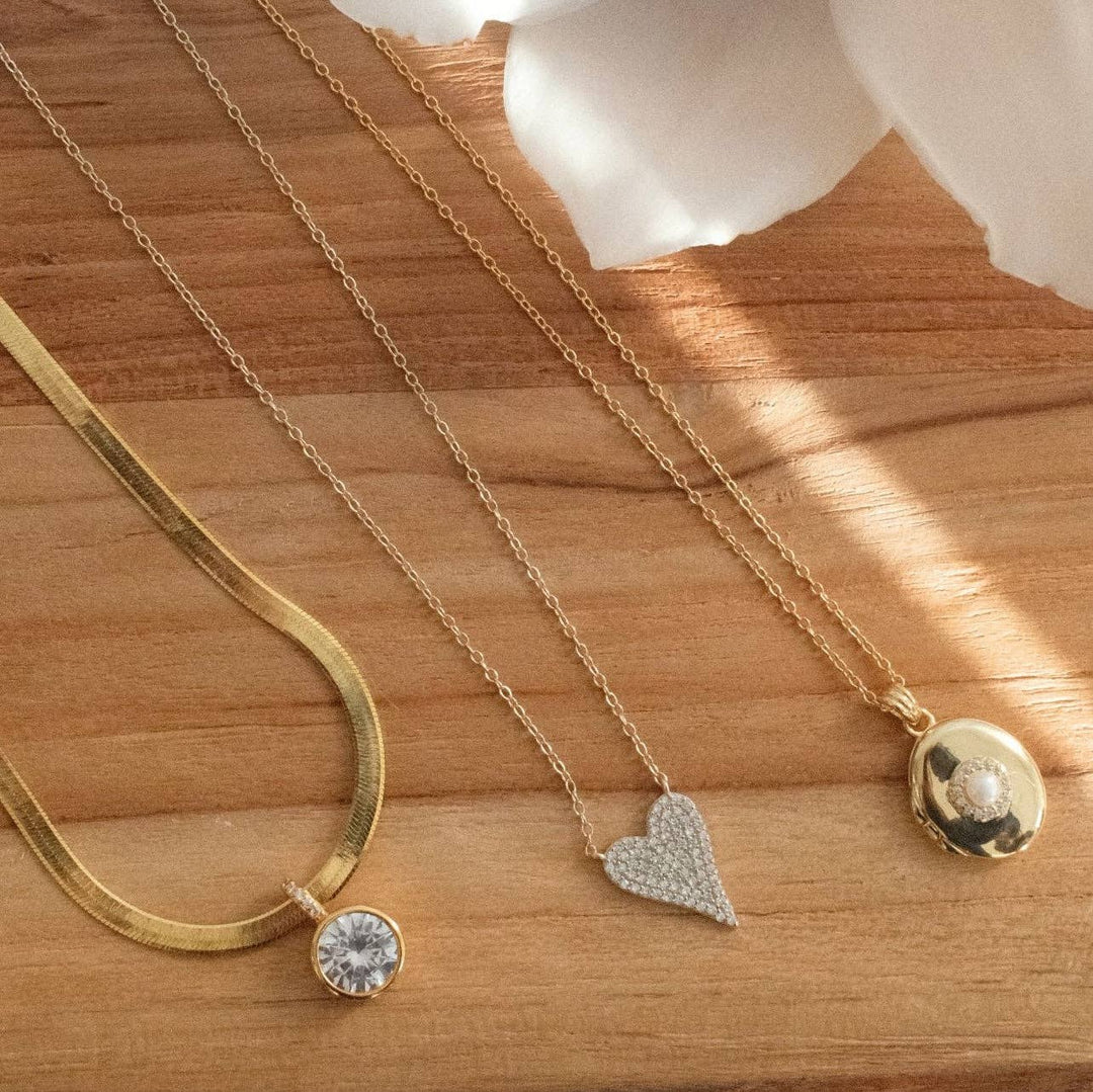 Three gold necklaces with various pendants on a wooden surface