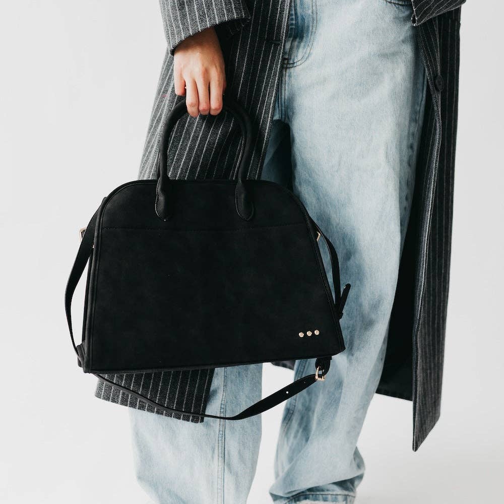 Person holding a black handbag with a neutral background
