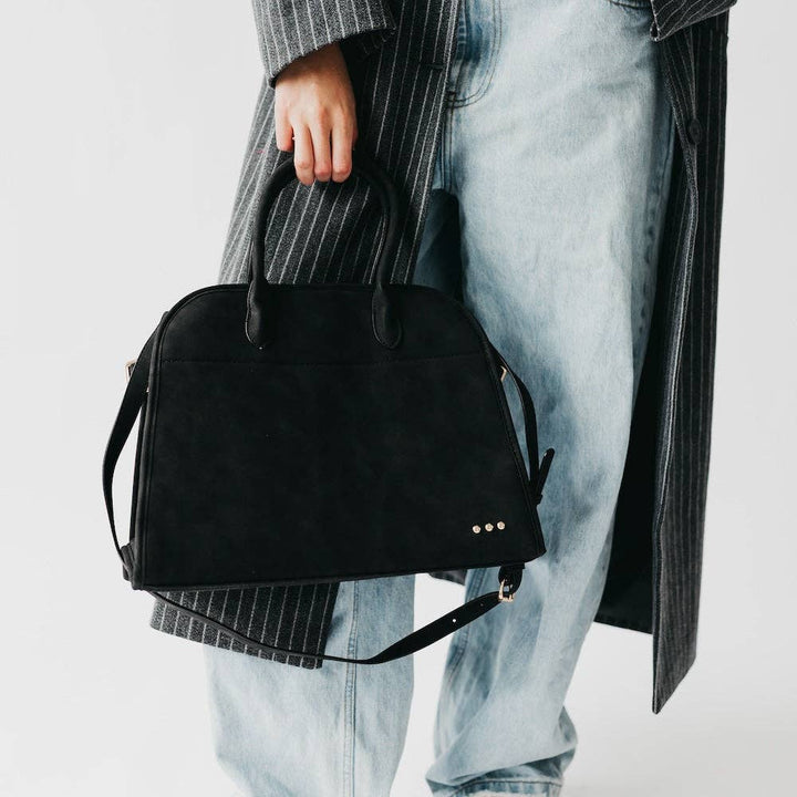 Person holding a black handbag with a neutral background