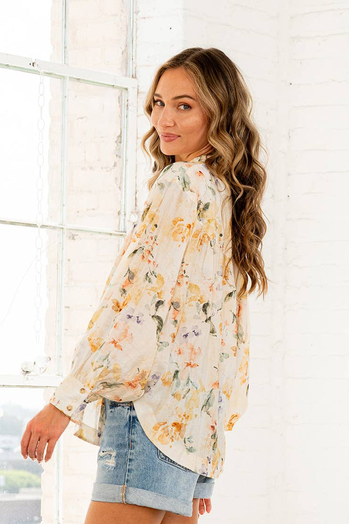 Woman wearing cream watercolor floral button-down blouse with long sleeves and denim shorts