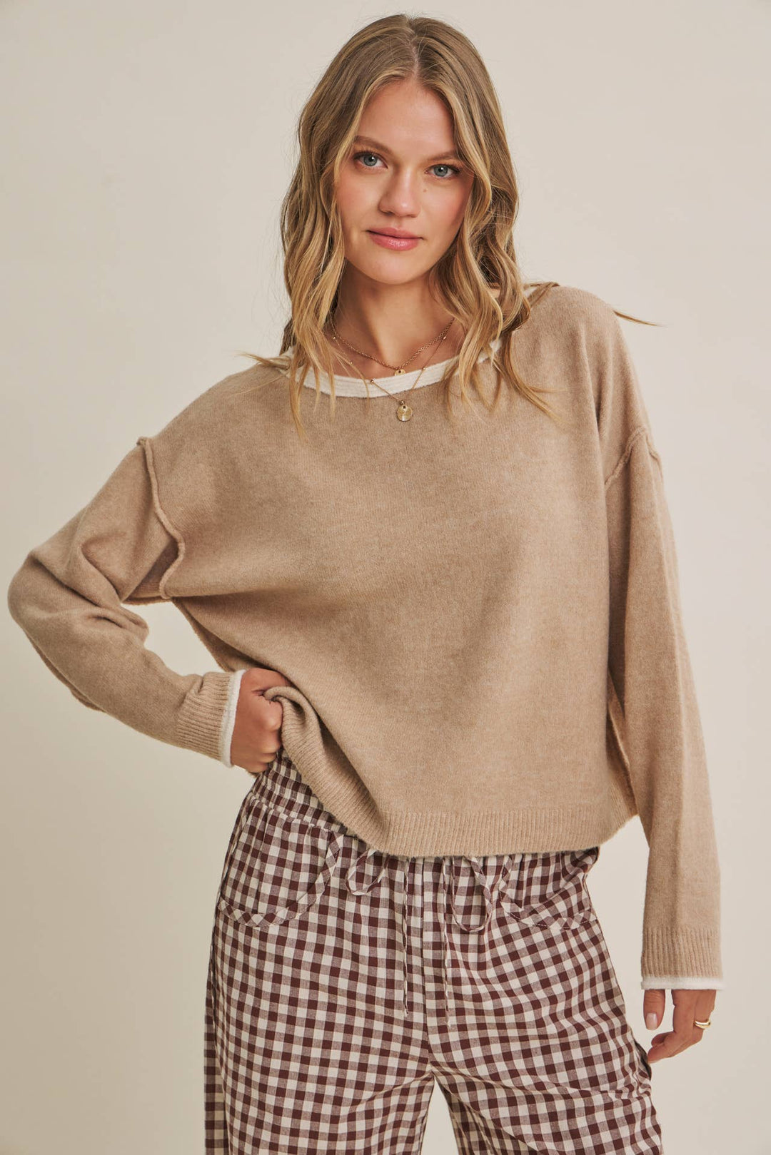 Woman wearing a beige sweater and plaid pants against a plain background