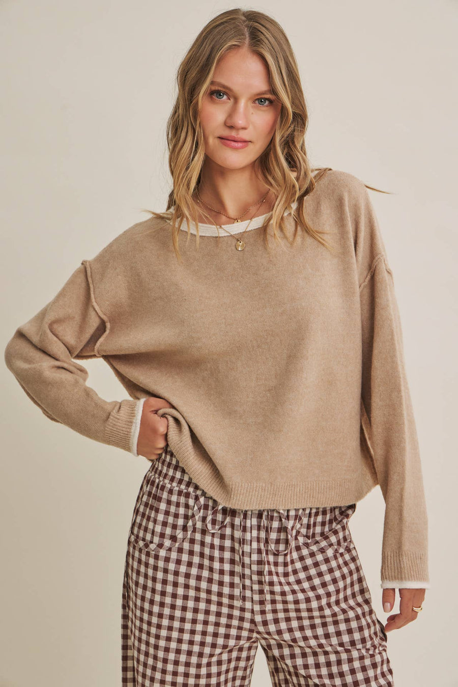 Woman wearing a beige sweater and plaid pants against a plain background
