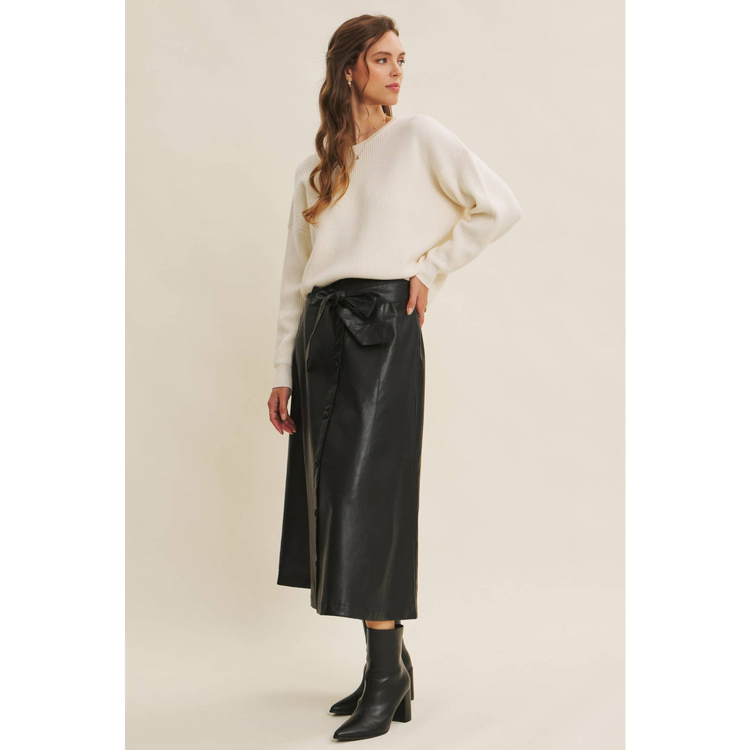 Woman wearing a Bow Back Sweater | Dolman Sleeve Knit with Satin Tie paired with a faux black leather skirt on a beige background. Side profile