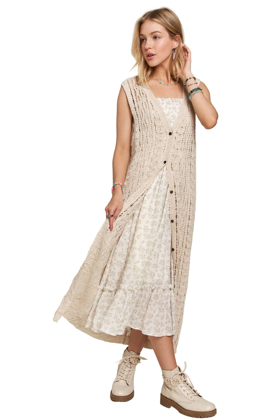 Woman wearing long beige crochet duster vest over a white floral dress