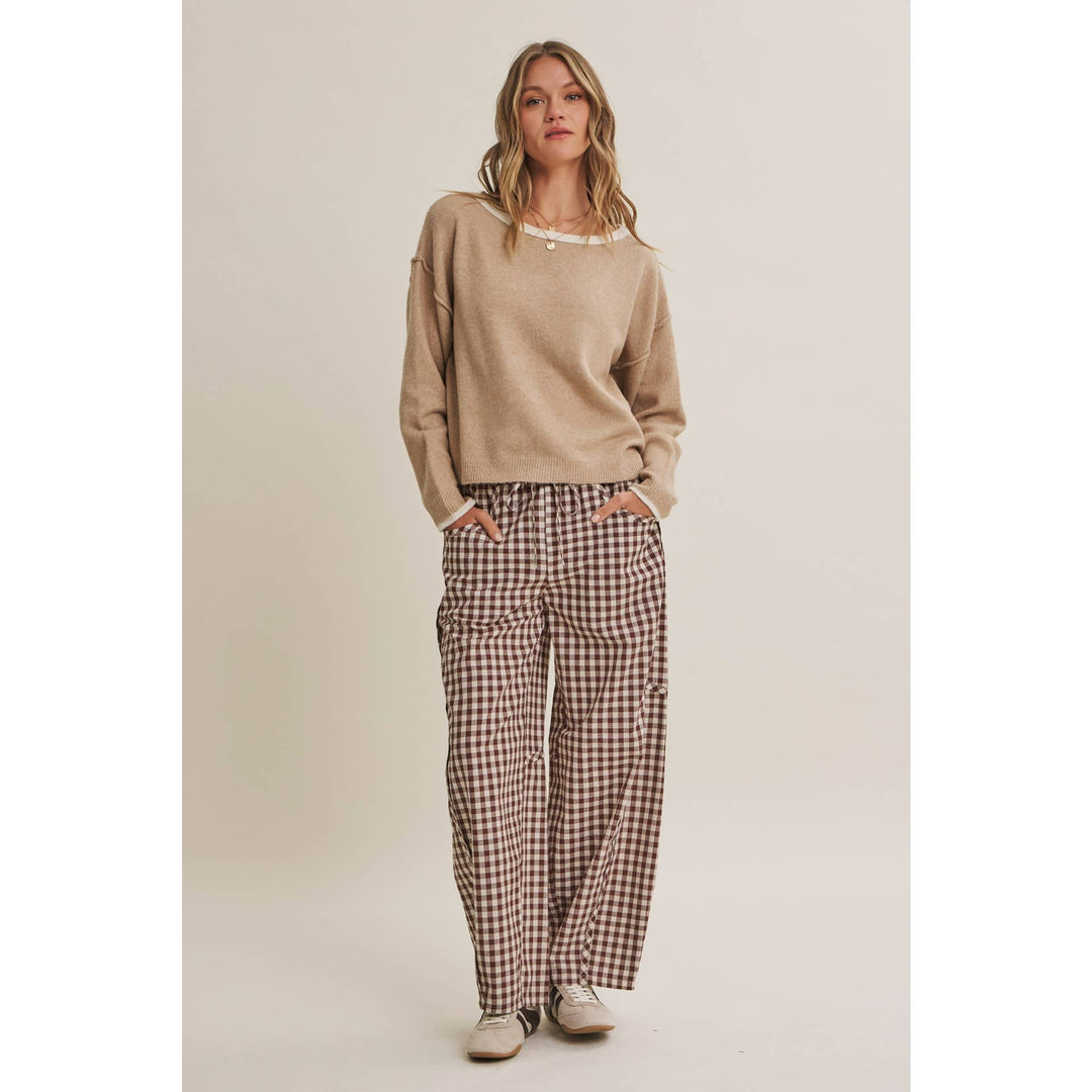 Woman wearing a beige sweater and plaid pants on a plain background