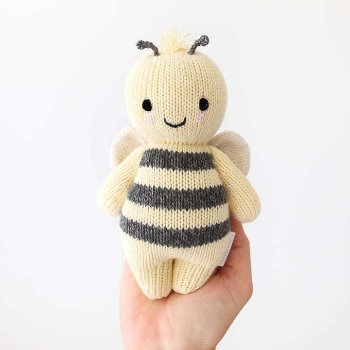 Knitted bee toy held in a hand against a white background