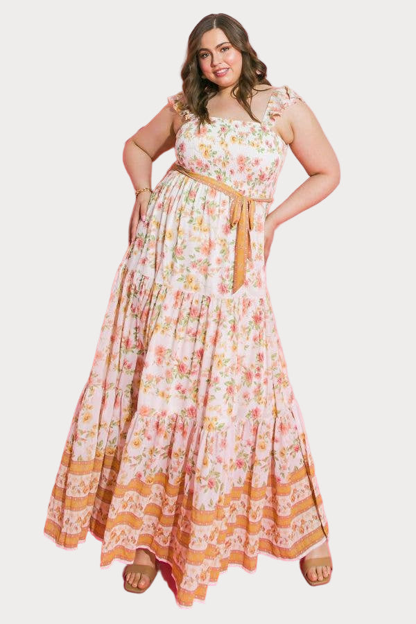 A model wearing a floral print maxi dress with a smocked bodice, sleeveless design, and a sash tie waist.