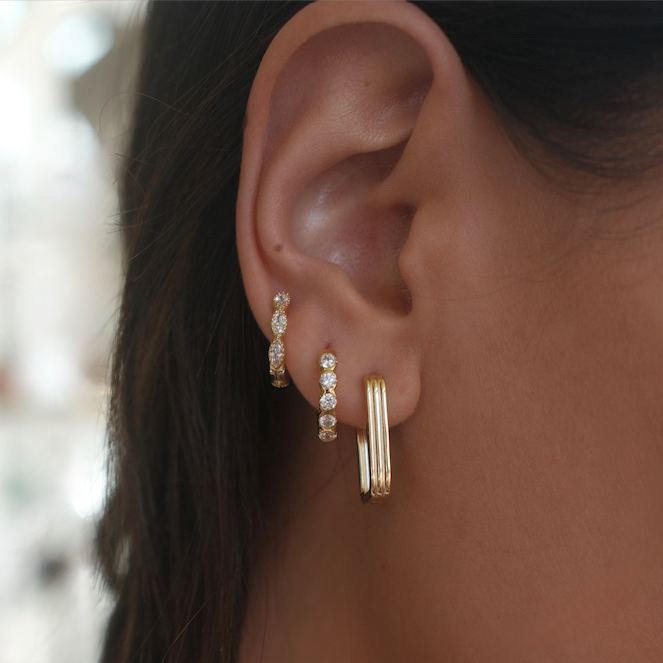 Close-up of an ear wearing gold hoop earrings with a blurred background
