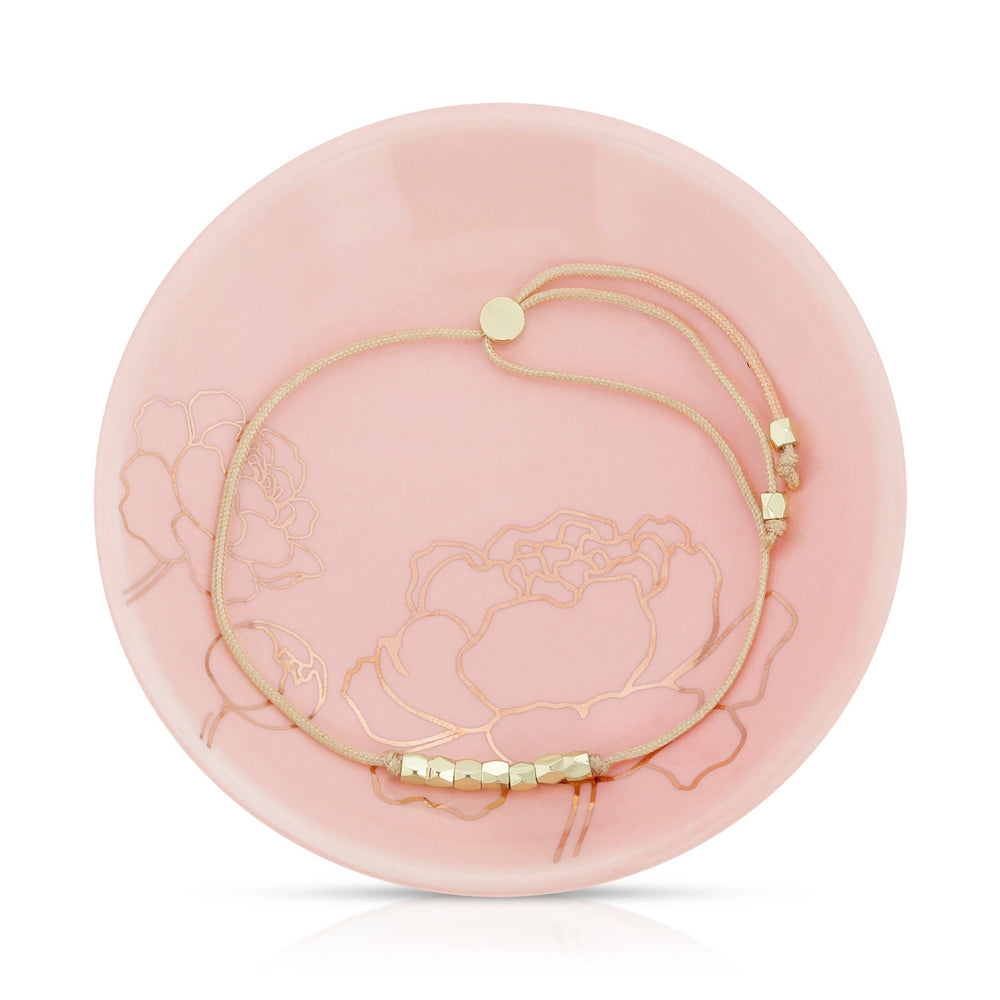 Gold bead & cord bracelet on a pink decorative dish with floral design