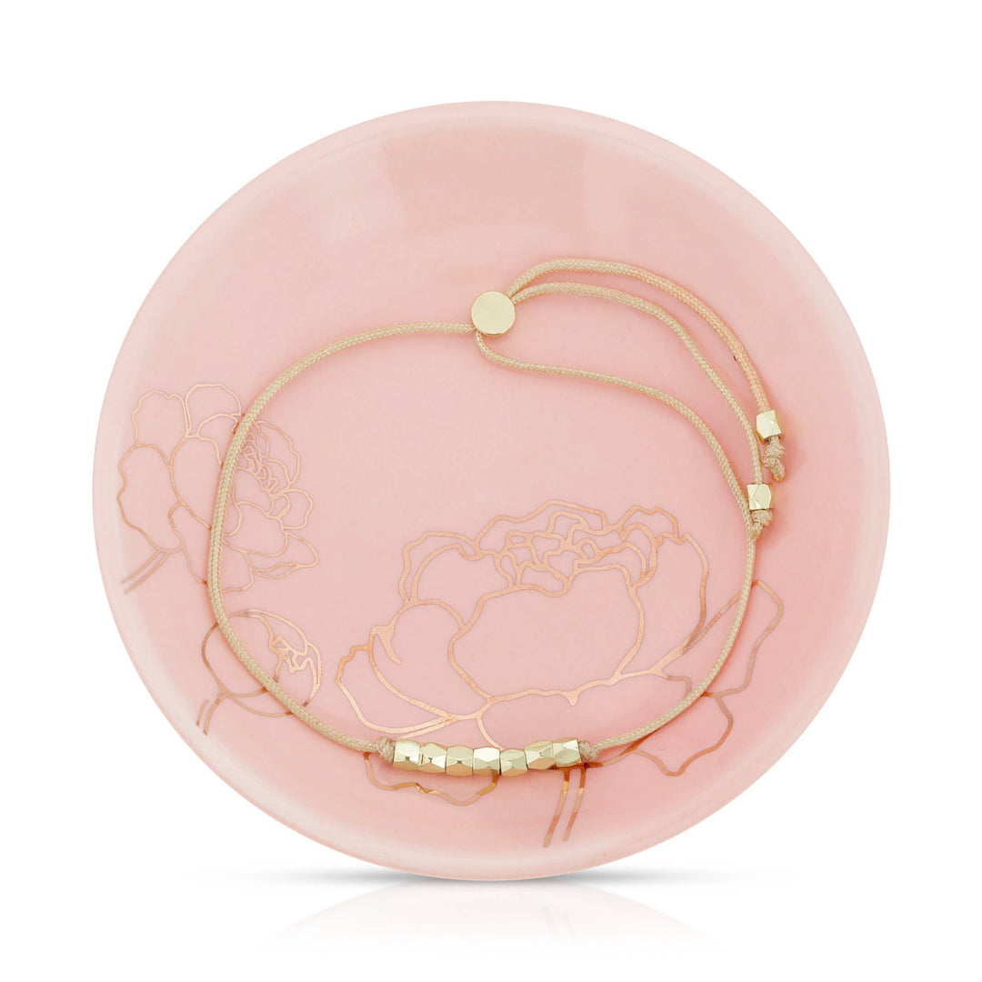 Gold bead & cord bracelet on a pink decorative dish with floral design