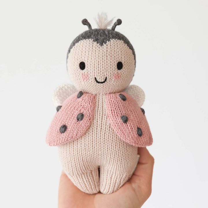 Knitted ladybug toy held by a hand on a white background