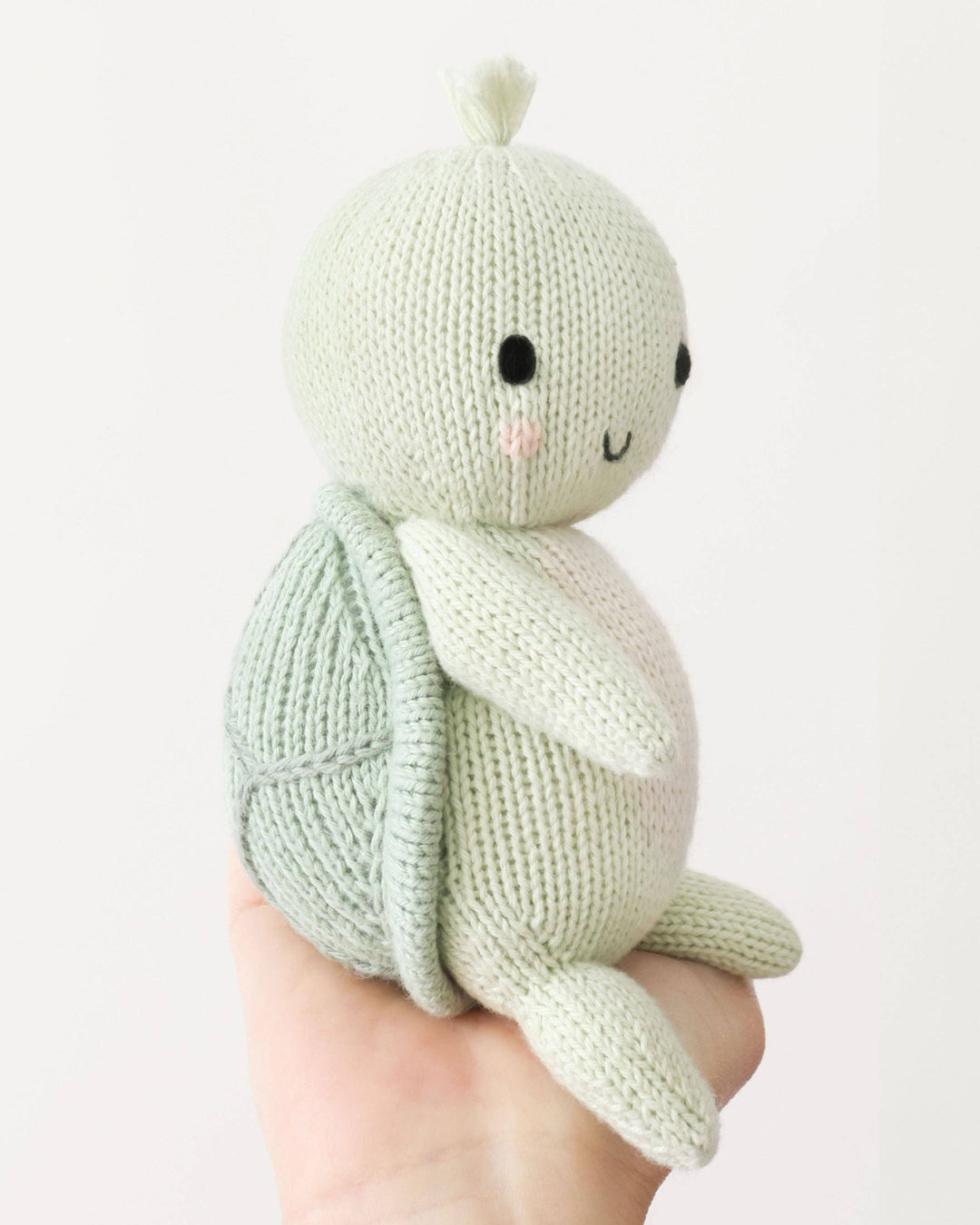 Knitted turtle toy held in a hand against a light background