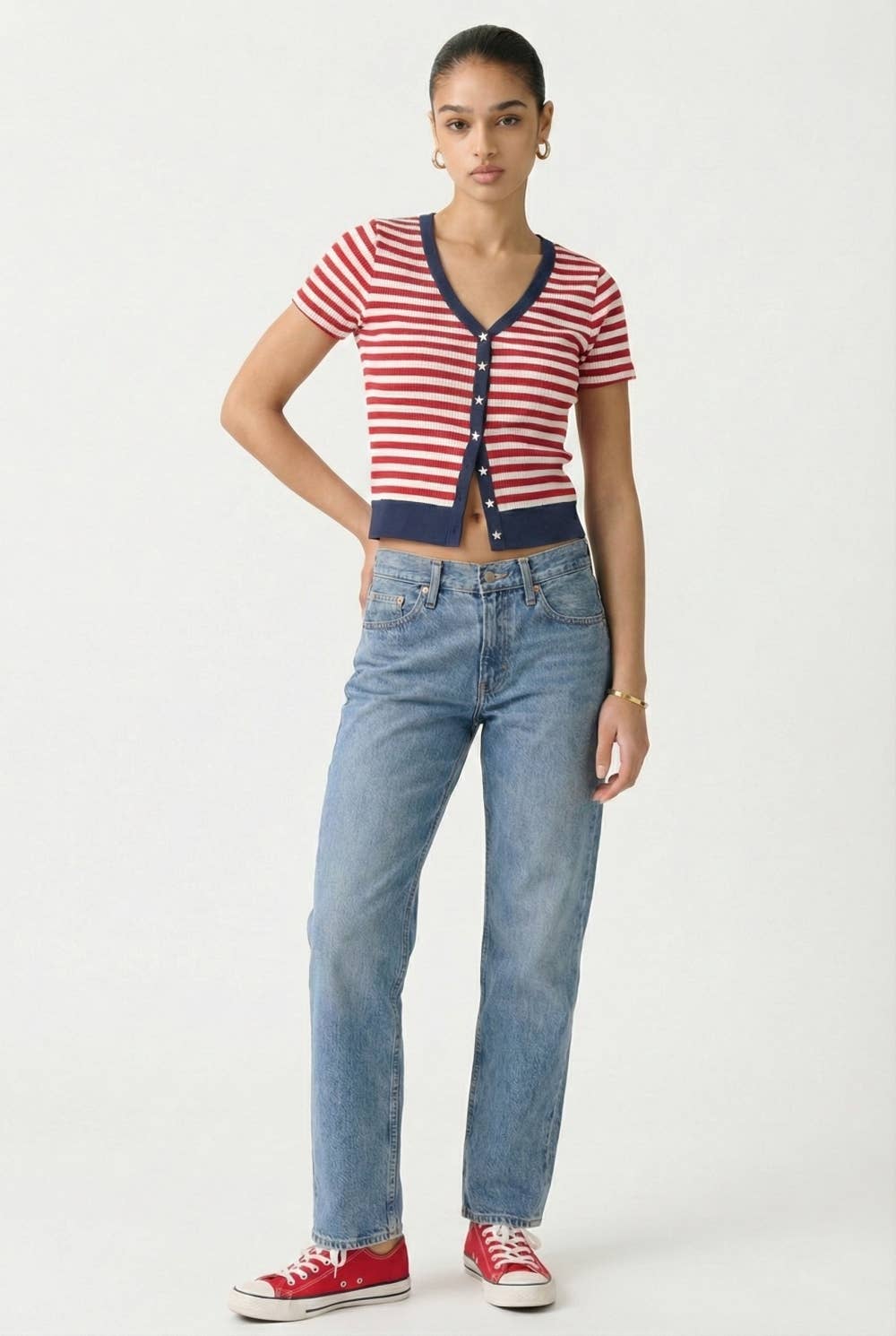 Woman wearing a red, white striped cardigan with navy trim & white star buttons and red sneakers on a white background