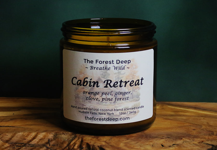 Amber glass candle labeled Cabin Retreat with orange, ginger, clove, and pine notes