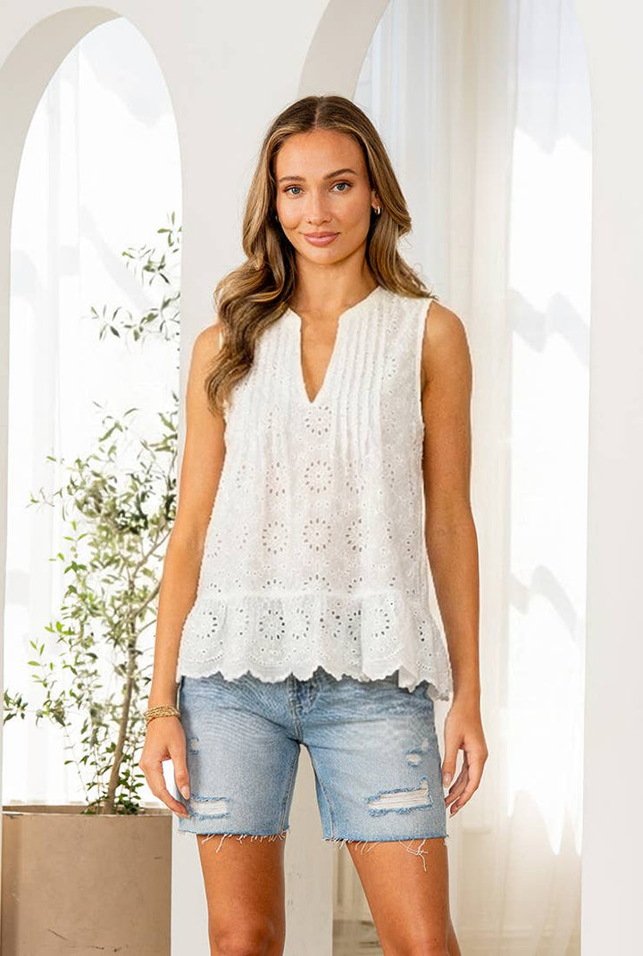 Woman wearing a white eyelet sleeveless top and denim shorts in a bright, sunlit room.