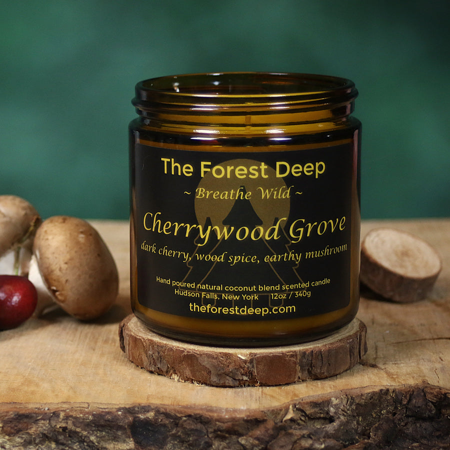 Candle jar labeled 'The Forest Deep Cherrywood Grove' on a wooden surface with cherries and mushrooms.
