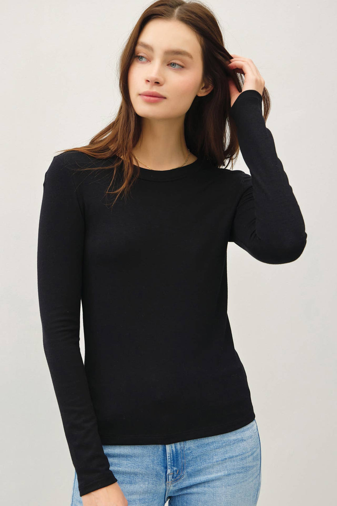 Woman wearing a black long-sleeve top and blue jeans on a light gray background