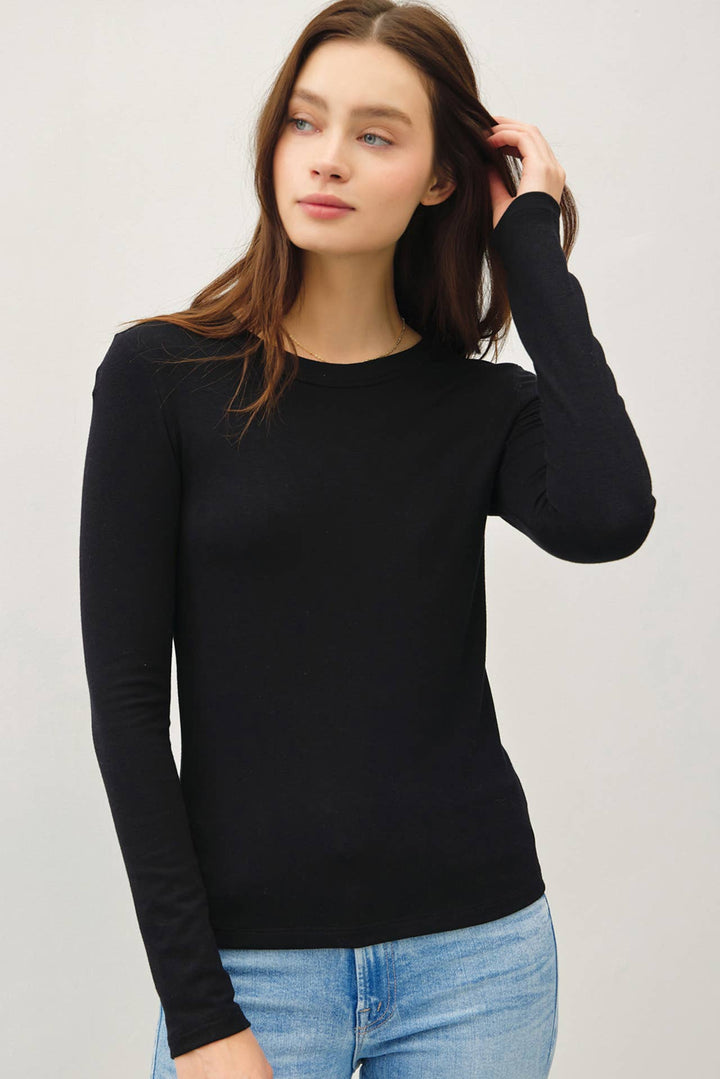 Woman wearing a black long-sleeve top and blue jeans on a light gray background