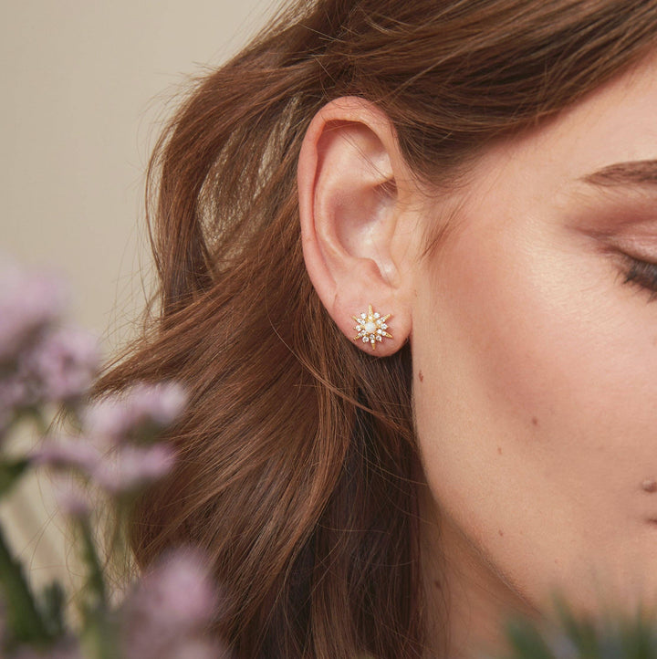 Model wearing Gold starburst opal stud earrings with cubic zirconia accents.