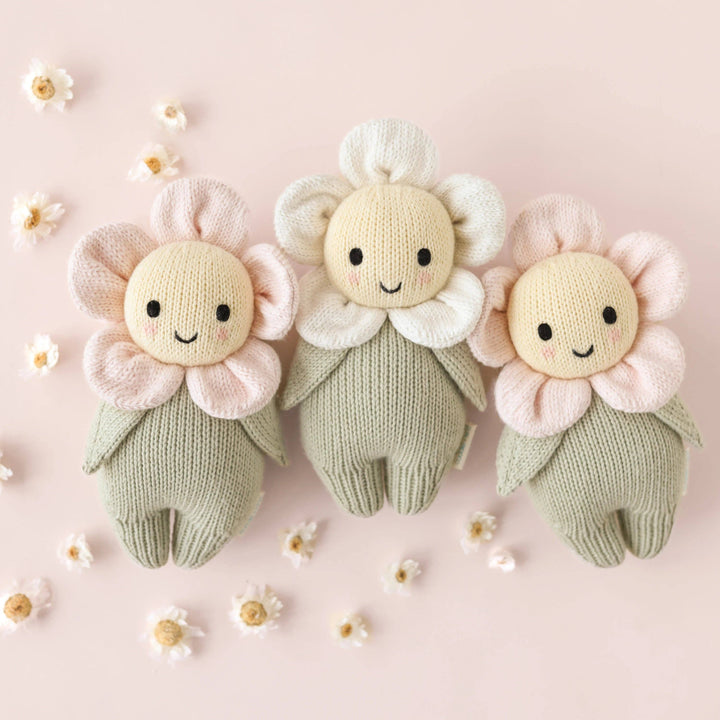 Three knitted flower toys on a pink background with small flowers around them.