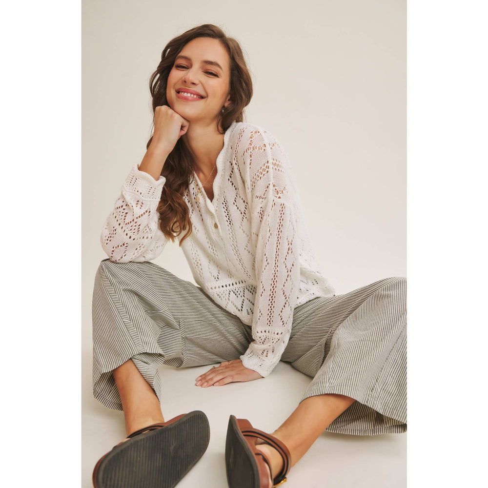 Woman wearing a white open-knit crochet sweater top with scalloped hem and long sleeves