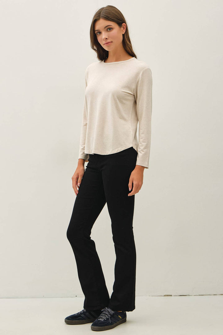 A woman modeling a cream-colored long-sleeve knit top and black pants against a plain white studio background.